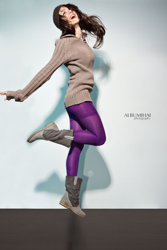 Dynamic studio portrait of Alice jumping mid-air in a brown sweater and purple tights during an editorial session.